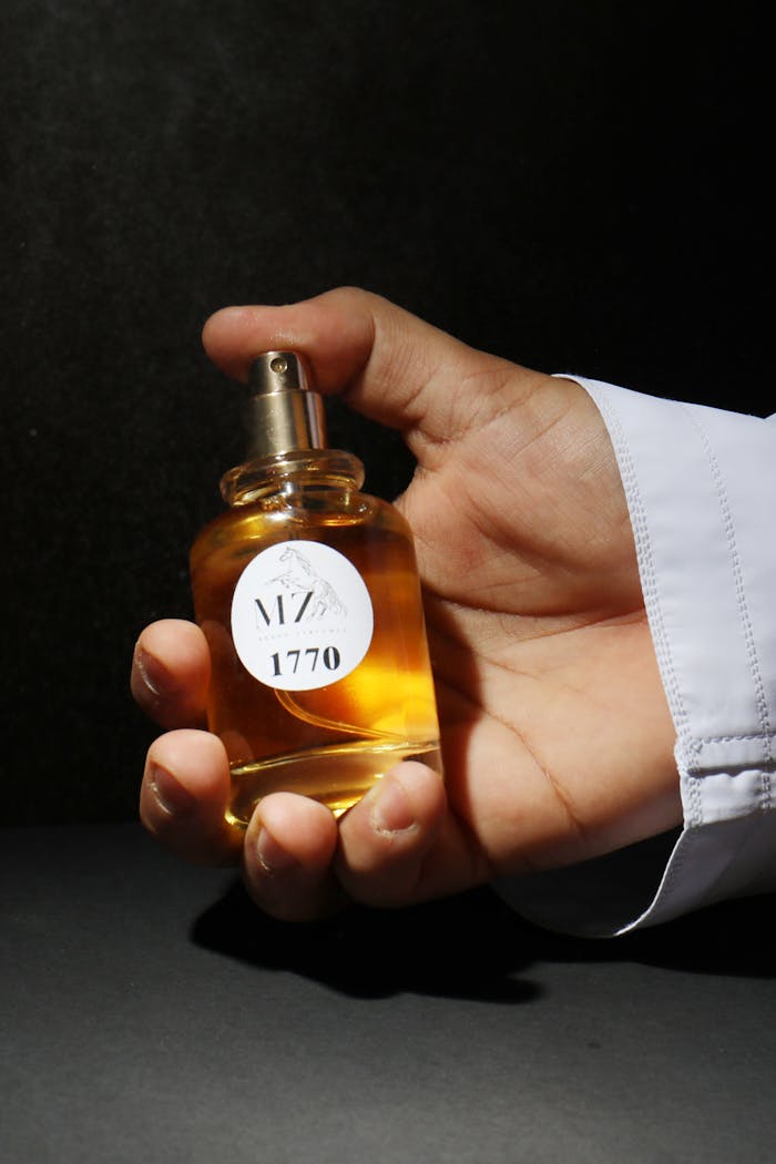 Close-up of a hand holding a perfume bottle with shadowed backdrop, emphasizing elegance.