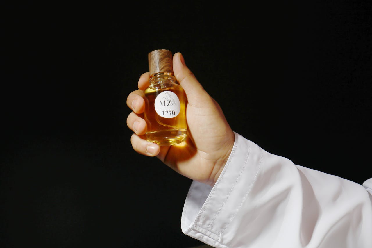 Close-up of a hand holding a luxurious perfume bottle against a dark background, capturing elegance.